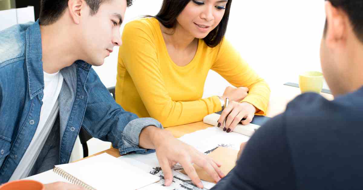 Three people looking over landscaping blueprints. Two people are facing forward, and the other has their back facing forward.