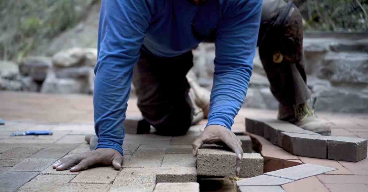 A professional brick paver kneeling on the ground and laying down bricks on the ground for a hardscaping project.