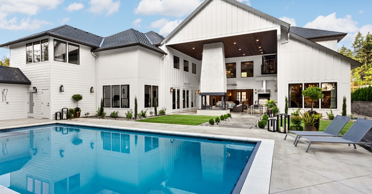 A large home with an open outdoor area that has a pool in the center. There’s a grill and firepit in the background.