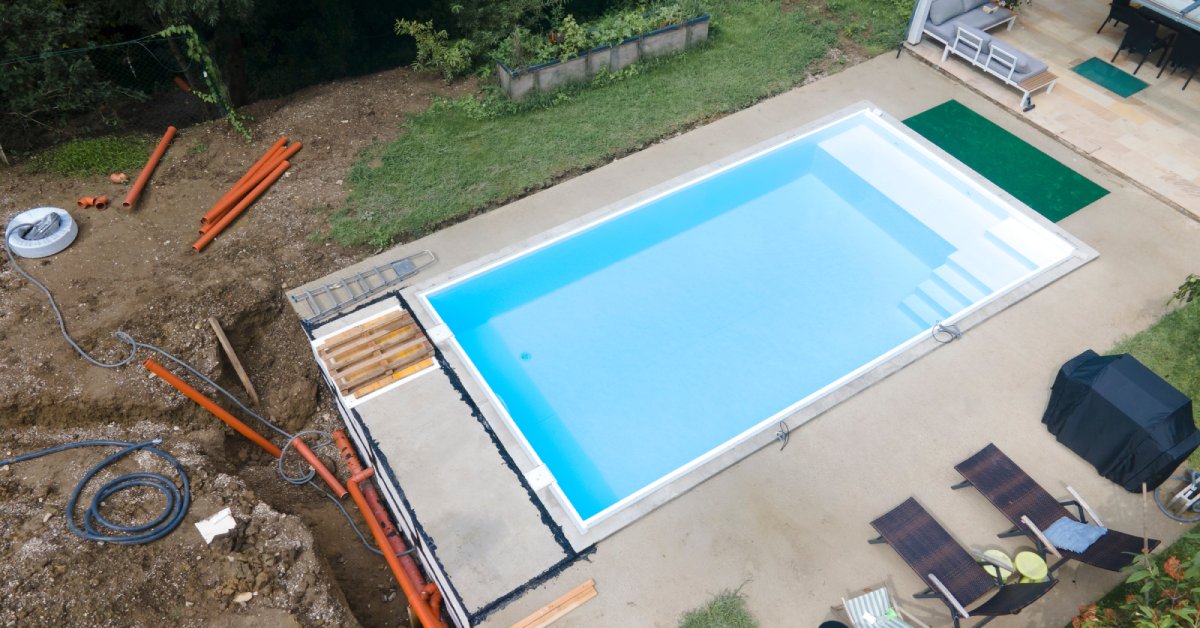 An overhead view of a newly constructed swimming pool in a backyard with pipes ready to be buried in the dirt.