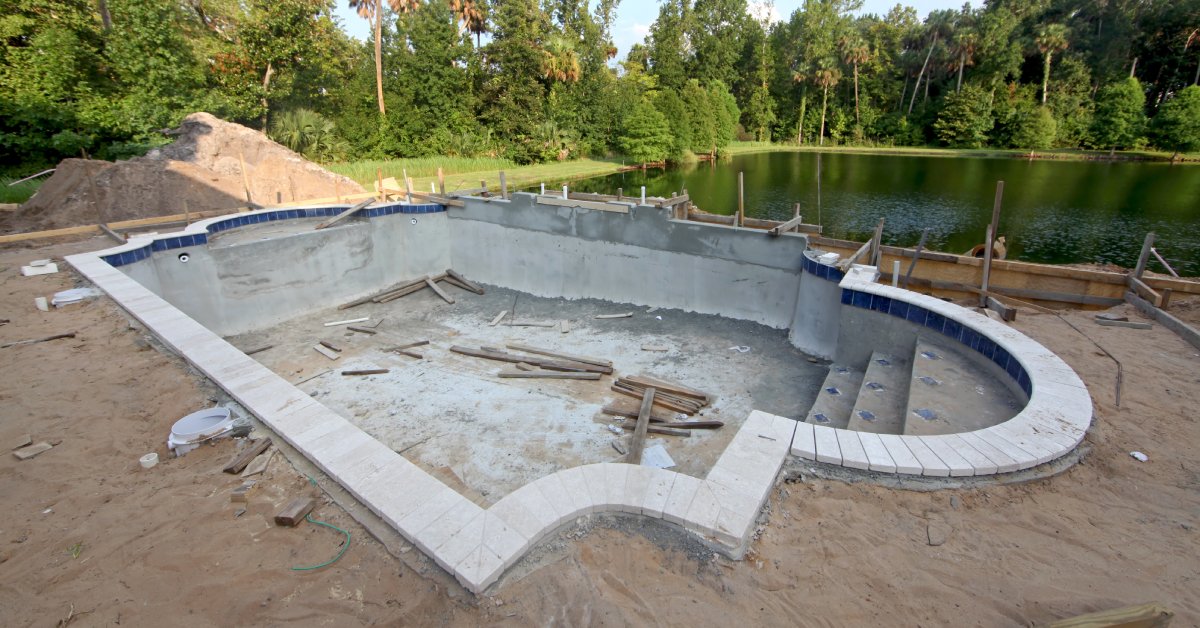 A swimming pool in the process of construction. The yard is torn up and there are construction materials lying around.