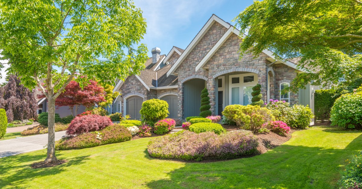 A luxurious home surrounded by a well-landscaped yard with vibrant trees and flower gardens scattered around.