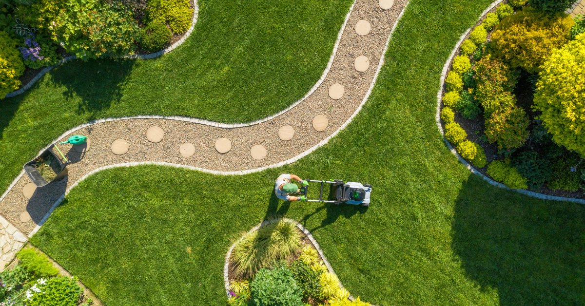 An overhead view of a well-landscaped yard with a person mowing and a curvy path with steppingstones going through the middle.
