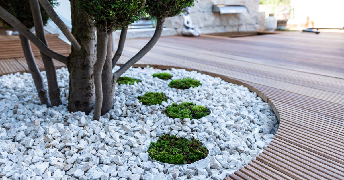 A patio with a Japanese Zen Garden built onto it. There’s an ornamental tree in the foreground and a fountain behind it.