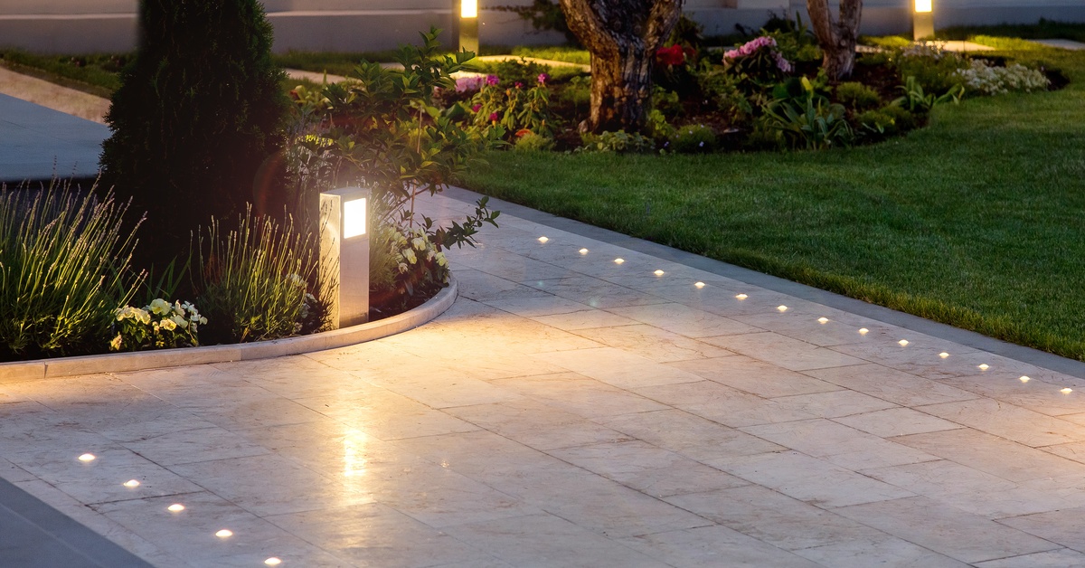 A marble walkway in a yard with LED lights embedded on the sides of the path. The trees have plants at their bases.